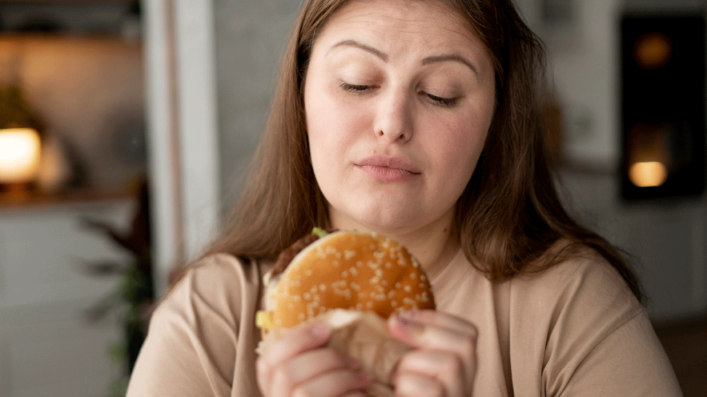 Beleibte Frau schaut kritisch auf einen Hambuger